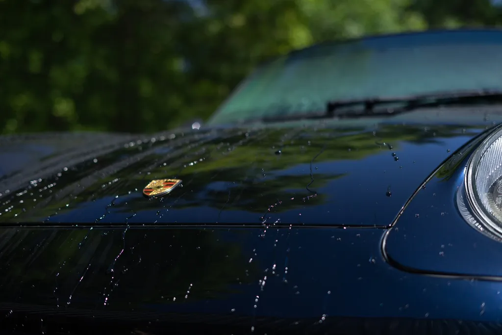 Water beading on the coated hood of a dark blue Porsche.