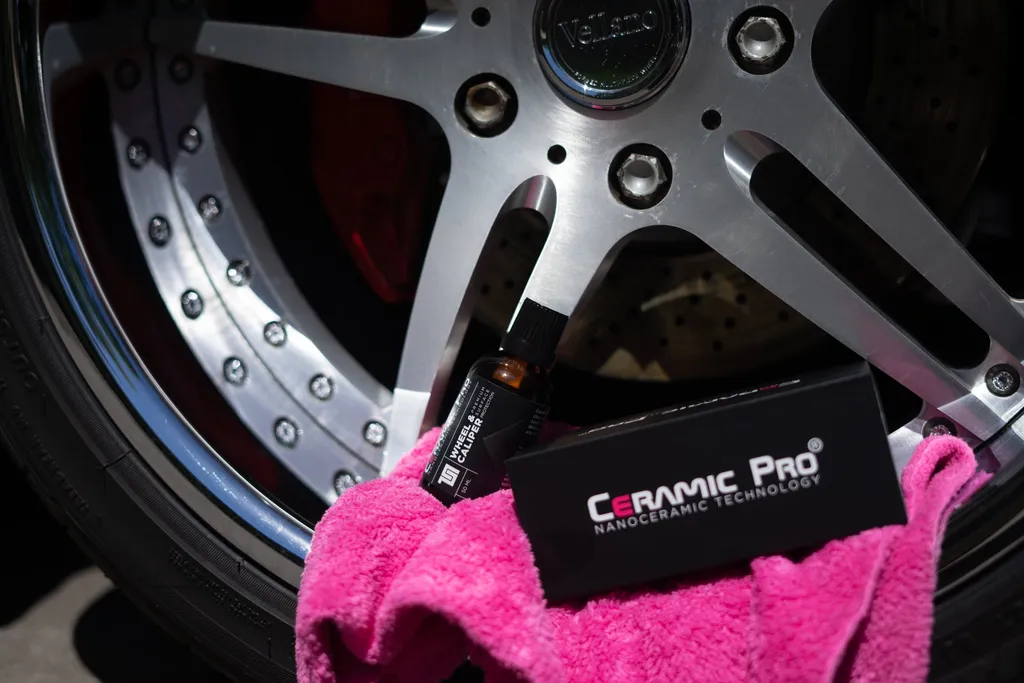 A Ceramic Pro coating kit and a pink microfiber towel against a polished wheel.