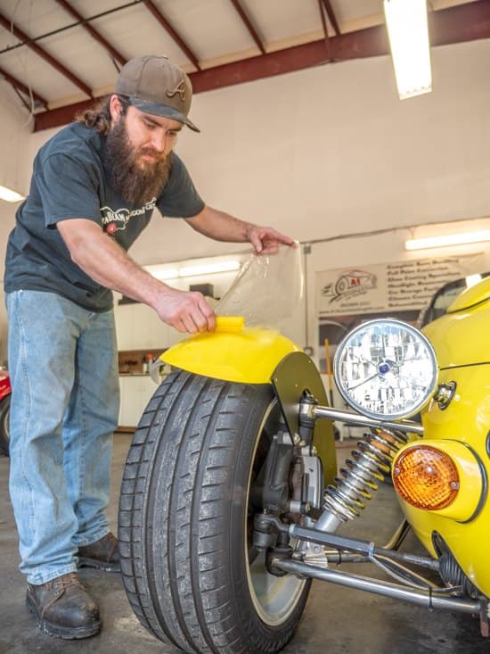 An A1 installer fitting clear protective film to the fender of a yellow roadster.