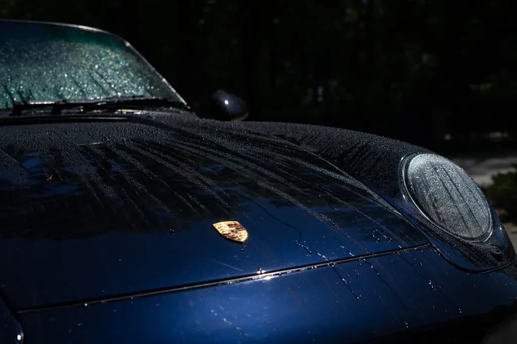 Rain beading across the coated hood and Porsche crest of a dark blue 911.