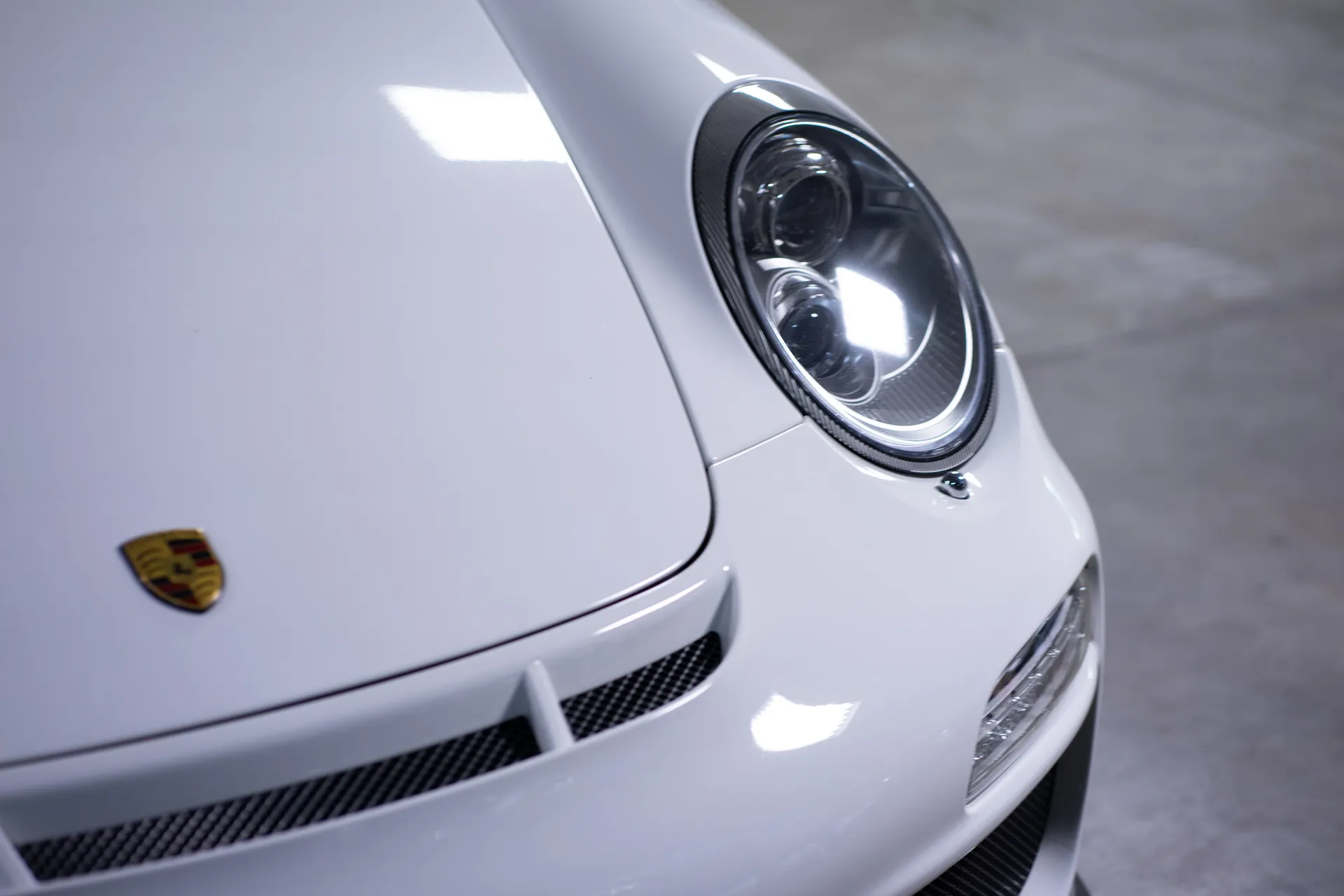 Close-up of the front badge and headlight of a white Porsche 911.