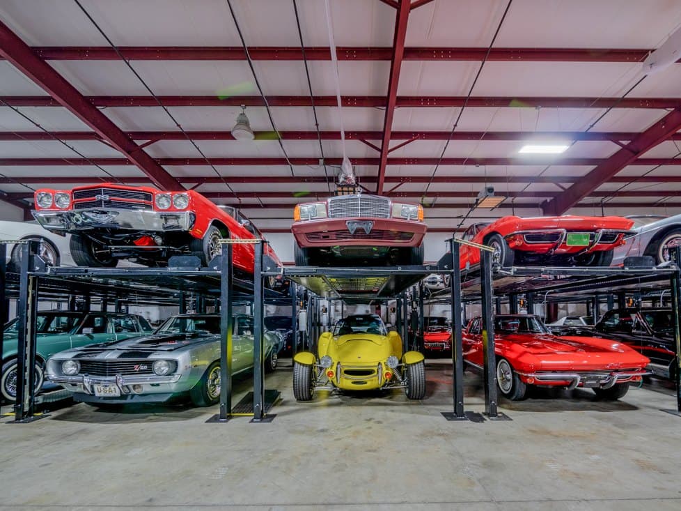 Two-level storage racks inside the A1 building: a red classic muscle car and a white sedan above, a yellow roadster and a red Corvette below.