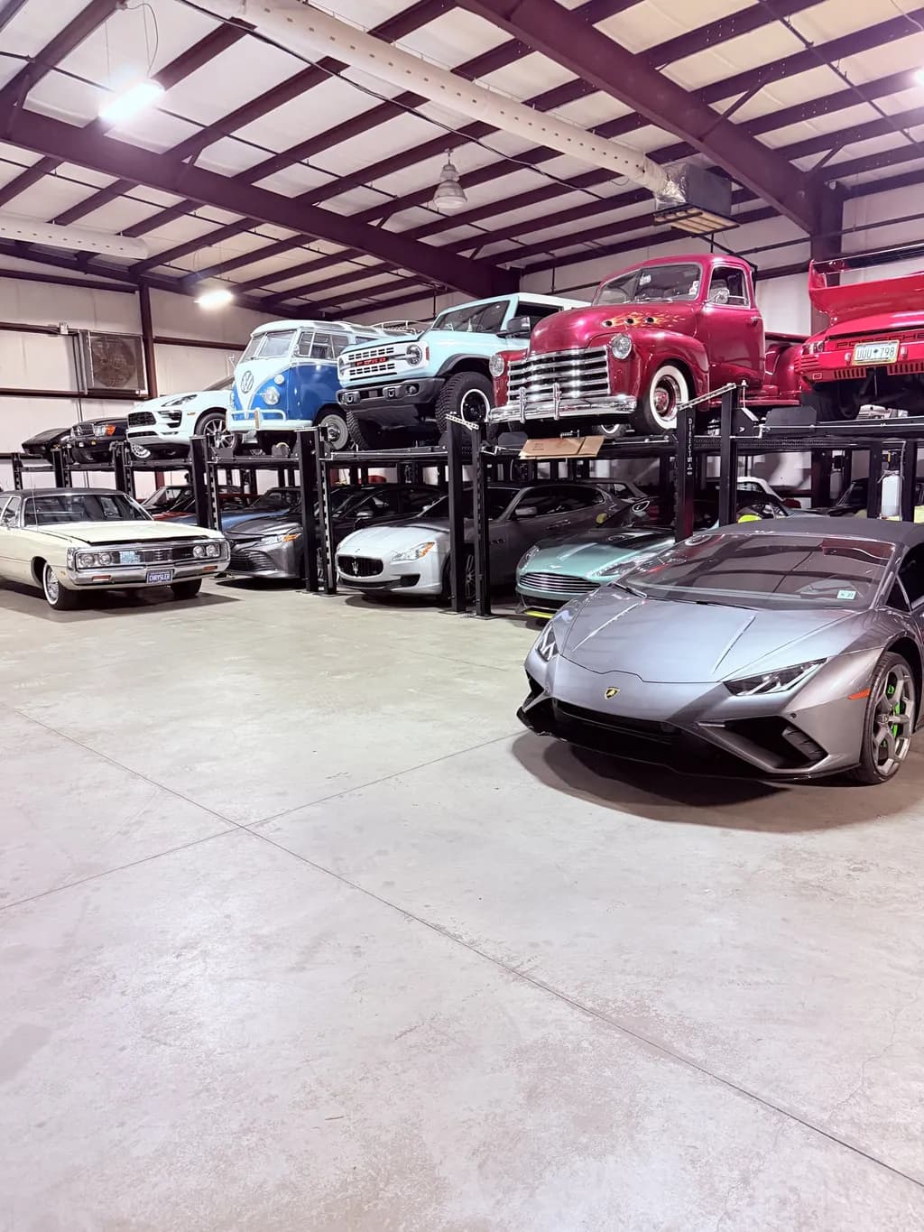 A gray Lamborghini on the storage floor, in front of racked classic trucks and convertibles.
