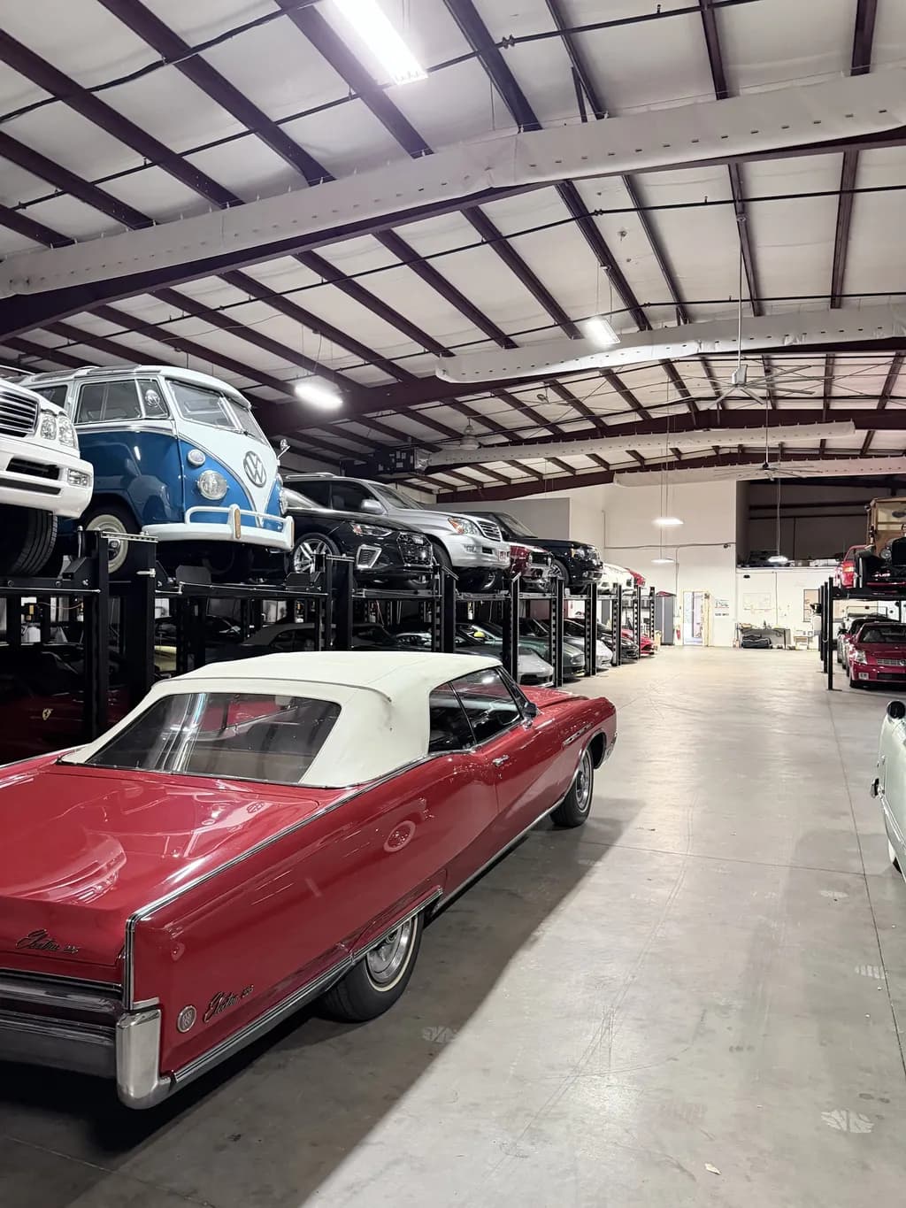 A red classic convertible in the aisle, with a Volkswagen bus and other cars racked behind it.