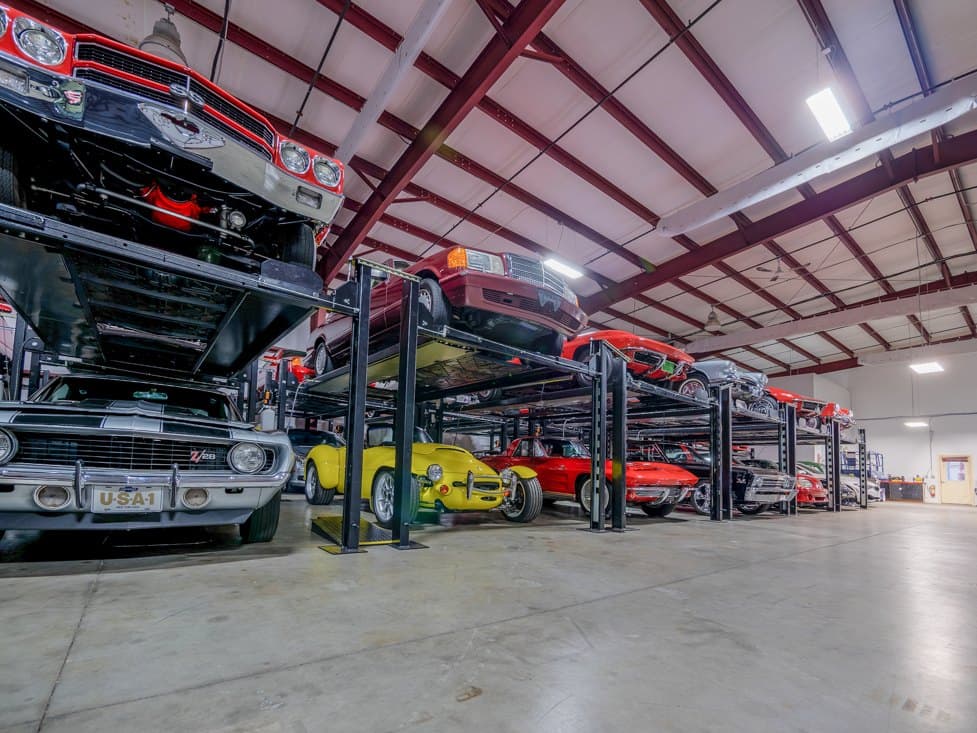 Classic muscle cars stored on two-level racks along a clean concrete floor.