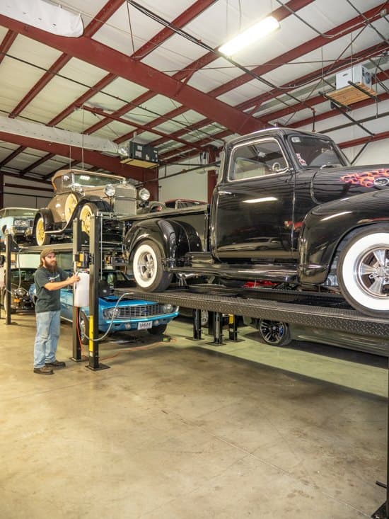An A1 technician working the lift that holds a black classic pickup truck in storage.